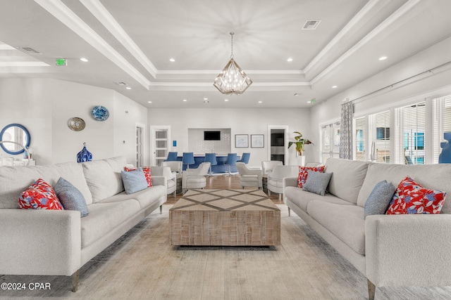 living room featuring an inviting chandelier, a tray ceiling, and light hardwood / wood-style floors