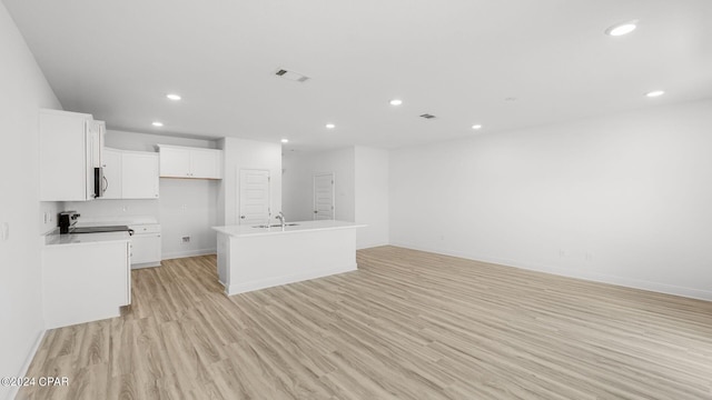 kitchen featuring light wood finished floors, recessed lighting, white cabinetry, stainless steel microwave, and open floor plan