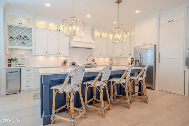 kitchen featuring white cabinets, a center island with sink, and stainless steel fridge