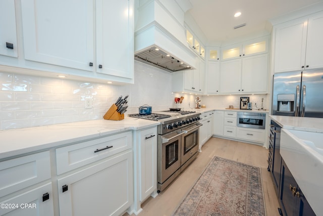 kitchen with custom range hood, decorative backsplash, white cabinetry, light stone countertops, and stainless steel appliances