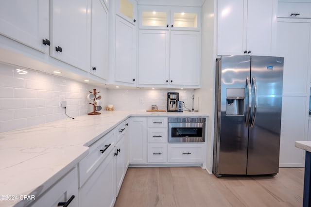 kitchen with light wood-type flooring, tasteful backsplash, white cabinetry, appliances with stainless steel finishes, and light stone countertops