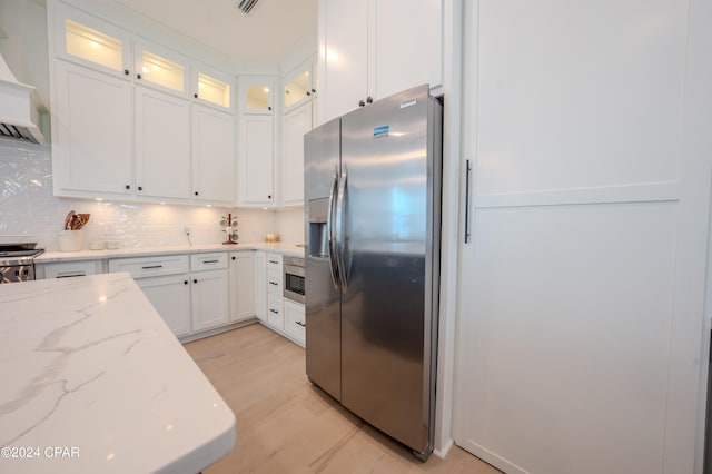 kitchen with white cabinetry, custom range hood, decorative backsplash, stainless steel appliances, and light stone countertops