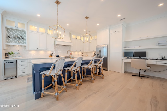 kitchen with stainless steel fridge, white cabinets, light wood-type flooring, custom exhaust hood, and decorative light fixtures