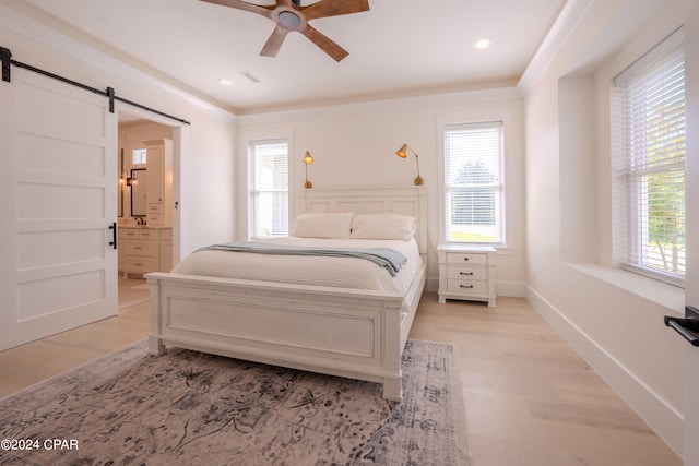 bedroom with multiple windows, ensuite bathroom, ceiling fan, and a barn door