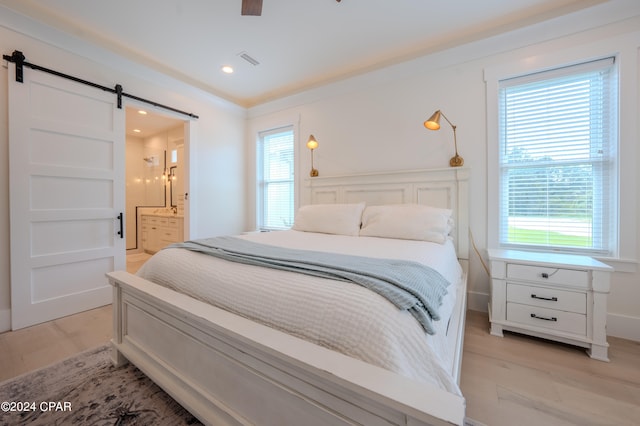 bedroom with light hardwood / wood-style floors, multiple windows, ensuite bathroom, and a barn door