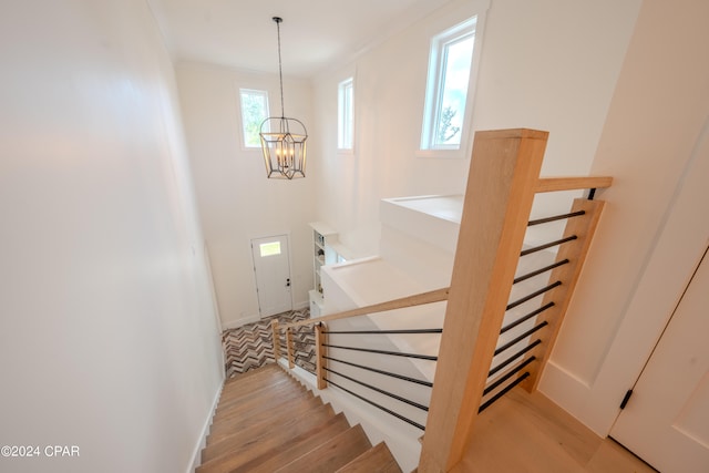 stairway with hardwood / wood-style flooring, a chandelier, and ornamental molding