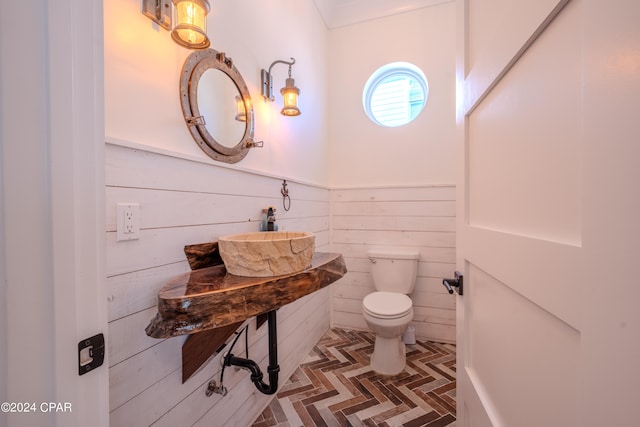 bathroom with parquet floors, wood walls, toilet, and sink