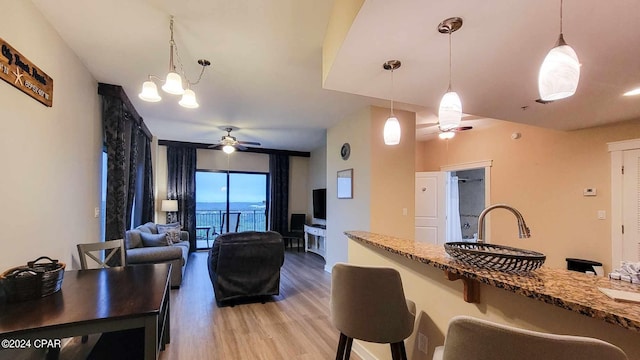 kitchen with stone counters, hardwood / wood-style floors, ceiling fan with notable chandelier, and hanging light fixtures