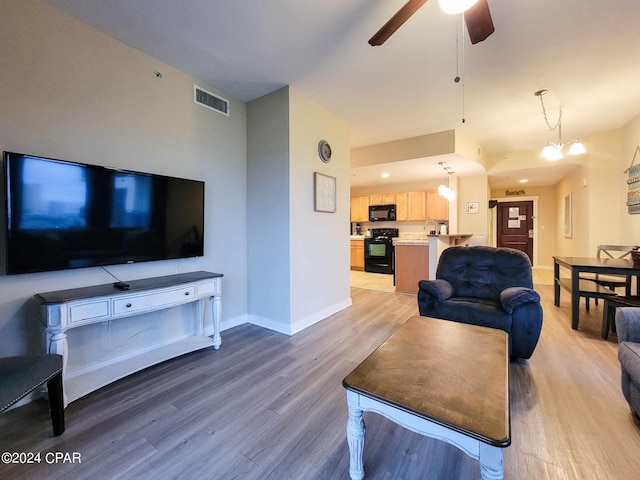 living room featuring ceiling fan with notable chandelier and hardwood / wood-style flooring