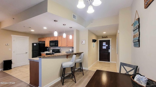 kitchen with black appliances, decorative light fixtures, light hardwood / wood-style floors, and stone countertops