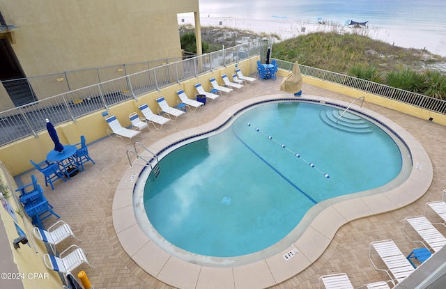 view of pool featuring a water view, a beach view, and a patio area