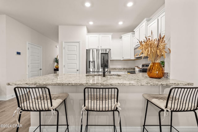 kitchen featuring light hardwood / wood-style floors, white cabinetry, kitchen peninsula, a kitchen bar, and stainless steel appliances