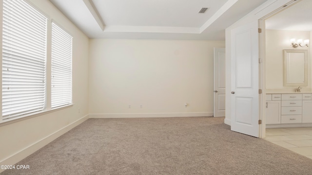 unfurnished bedroom with a tray ceiling, ensuite bath, and light carpet