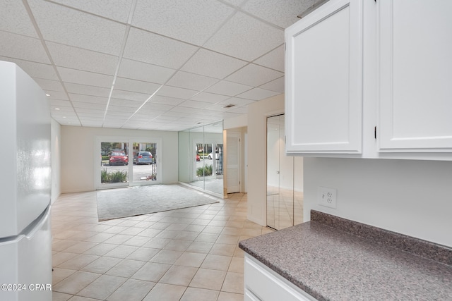 kitchen with light tile patterned floors, a drop ceiling, white fridge, and white cabinetry