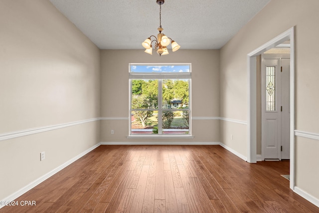 spare room with a textured ceiling, hardwood / wood-style floors, and a chandelier