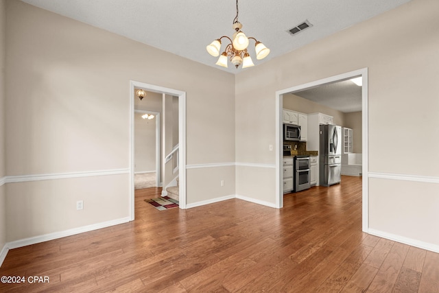 spare room with a textured ceiling, an inviting chandelier, and hardwood / wood-style flooring