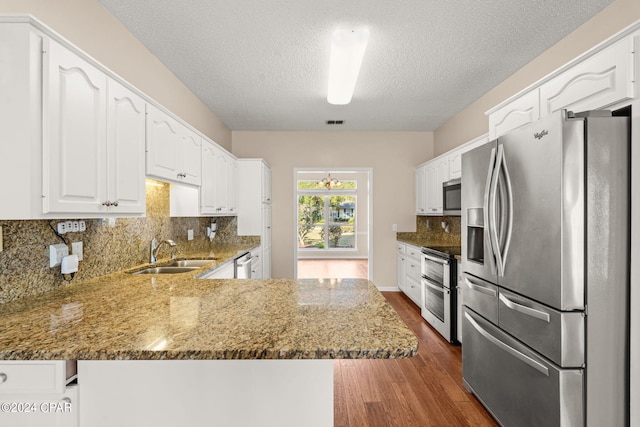 kitchen with white cabinets, sink, kitchen peninsula, appliances with stainless steel finishes, and dark hardwood / wood-style floors