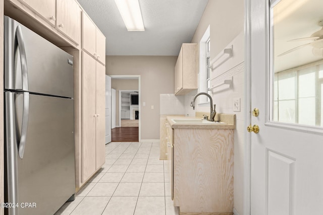 kitchen featuring ceiling fan, light tile patterned floors, sink, a textured ceiling, and stainless steel refrigerator