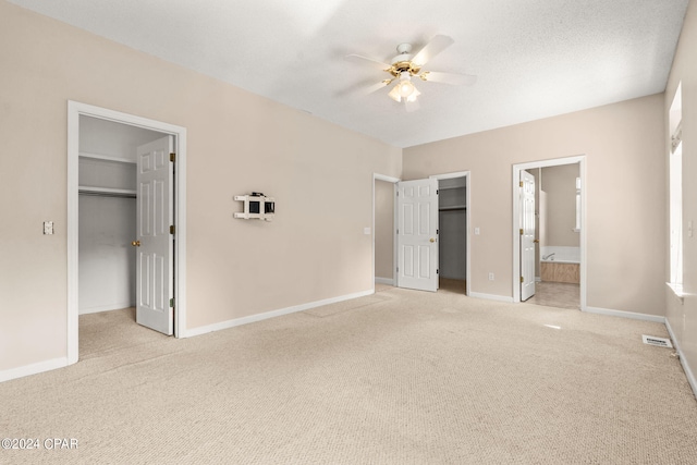 unfurnished bedroom with ceiling fan, connected bathroom, a closet, a spacious closet, and light colored carpet