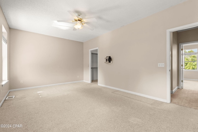 empty room with ceiling fan, a textured ceiling, and light carpet