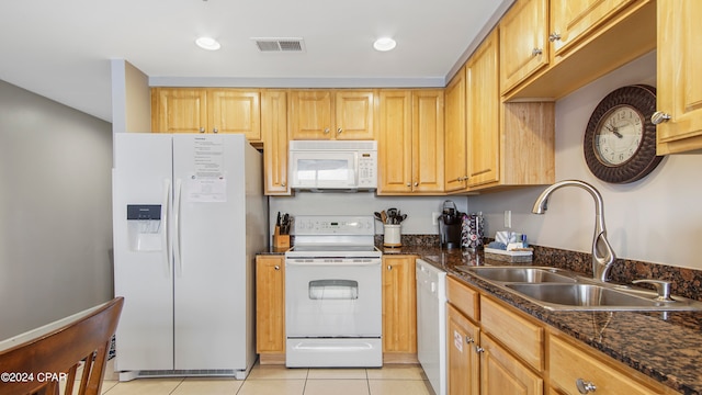 kitchen with light tile patterned floors, light brown cabinetry, sink, dark stone countertops, and white appliances