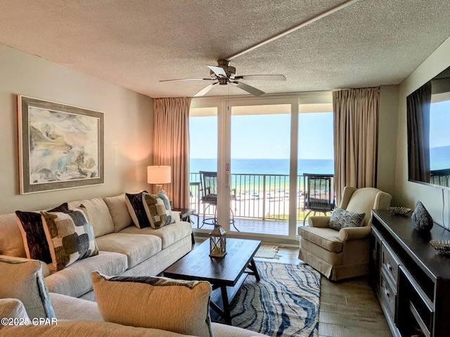 living room with a view of the beach, a water view, a textured ceiling, hardwood / wood-style flooring, and ceiling fan