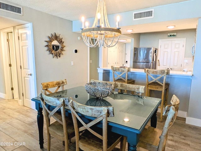 dining area with a notable chandelier, a textured ceiling, and light hardwood / wood-style flooring