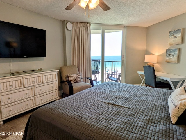 bedroom with a water view, a textured ceiling, access to outside, dark hardwood / wood-style floors, and ceiling fan