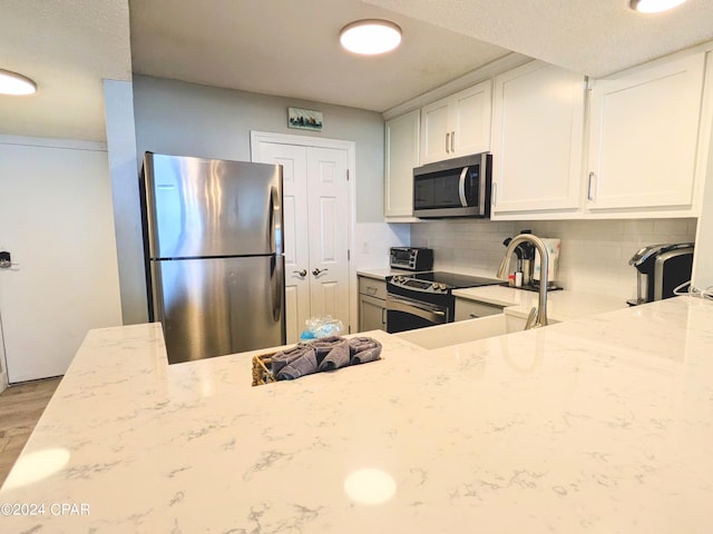 kitchen featuring white cabinetry, stainless steel appliances, light stone countertops, decorative backsplash, and light wood-type flooring