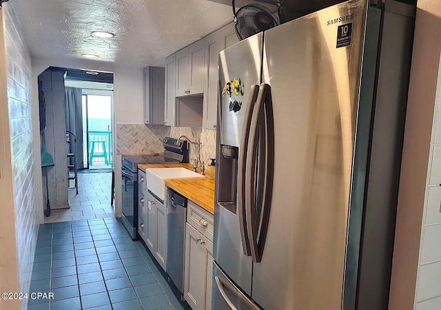 kitchen featuring appliances with stainless steel finishes, decorative backsplash, light tile patterned floors, wooden counters, and a textured ceiling