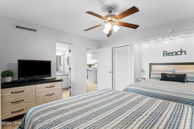 bedroom with ceiling fan, light tile patterned floors, a textured ceiling, a closet, and ensuite bath