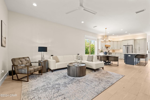 living room featuring ceiling fan with notable chandelier, sink, and light hardwood / wood-style flooring