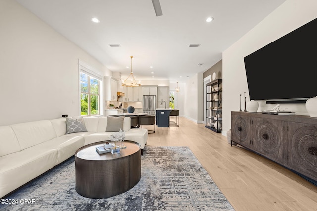 living room with an inviting chandelier, light hardwood / wood-style flooring, and sink