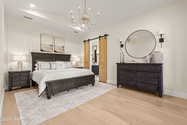 bedroom with an inviting chandelier, a barn door, light hardwood / wood-style flooring, ensuite bathroom, and vaulted ceiling