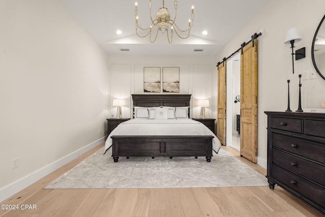 bedroom featuring a barn door, light hardwood / wood-style floors, an inviting chandelier, and lofted ceiling