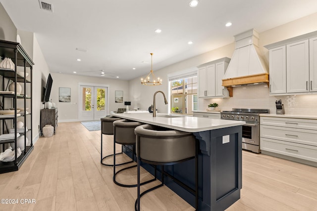 kitchen with high end stove, white cabinetry, a kitchen island with sink, and premium range hood