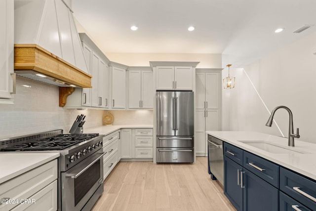 kitchen with premium range hood, blue cabinets, sink, tasteful backsplash, and stainless steel appliances