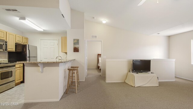 kitchen featuring appliances with stainless steel finishes, a breakfast bar, kitchen peninsula, lofted ceiling, and light colored carpet