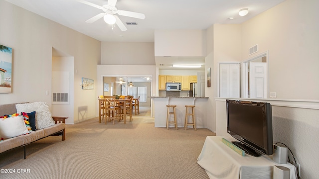 carpeted living room featuring a towering ceiling and ceiling fan