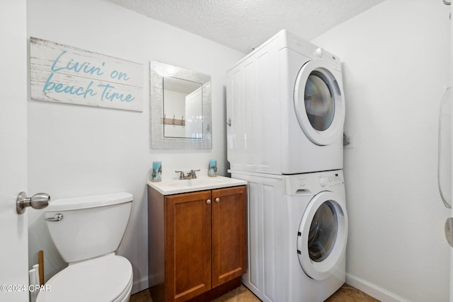 clothes washing area with a textured ceiling, sink, and stacked washing maching and dryer