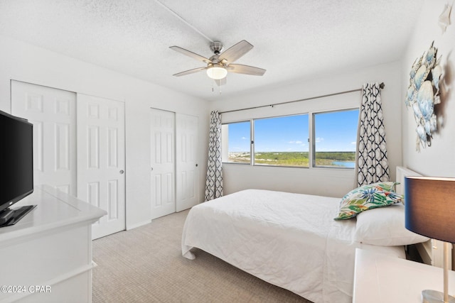 bedroom with a textured ceiling, two closets, ceiling fan, and light carpet