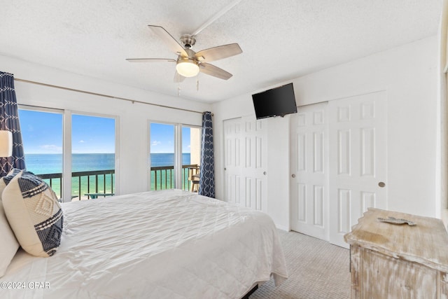 carpeted bedroom with a water view, a textured ceiling, access to exterior, and ceiling fan