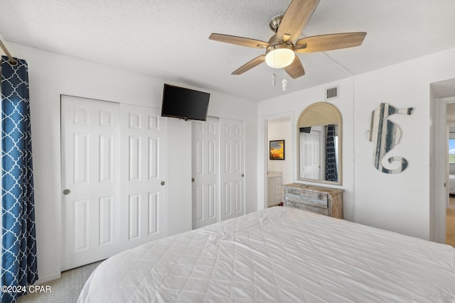 bedroom featuring ceiling fan, light colored carpet, a textured ceiling, and two closets