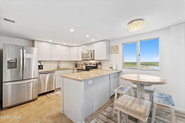 kitchen featuring light stone counters, light tile patterned floors, kitchen peninsula, white cabinetry, and appliances with stainless steel finishes