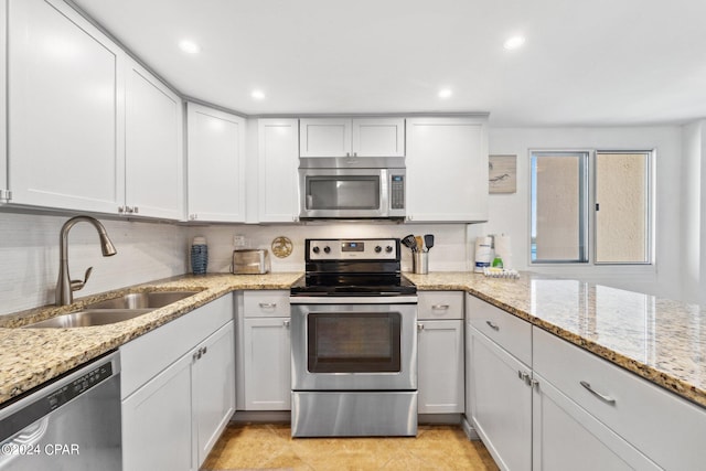 kitchen featuring light stone counters, white cabinets, stainless steel appliances, and sink