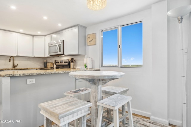 kitchen featuring light wood-type flooring, light stone counters, white cabinets, a kitchen bar, and appliances with stainless steel finishes