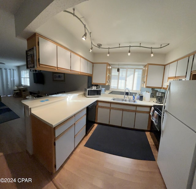 kitchen with light countertops, a sink, light wood-type flooring, a peninsula, and black appliances