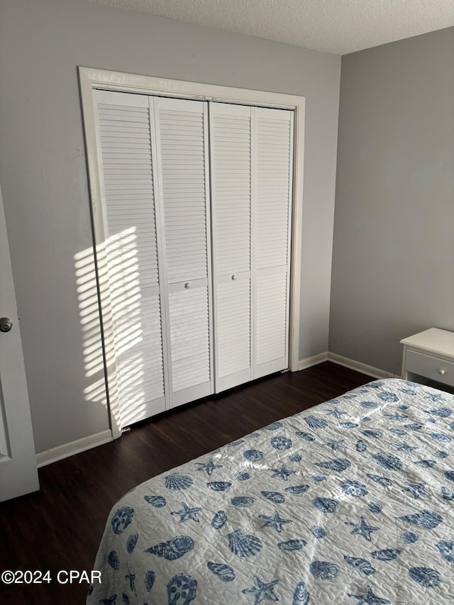 bedroom featuring a closet, dark wood finished floors, a textured ceiling, and baseboards