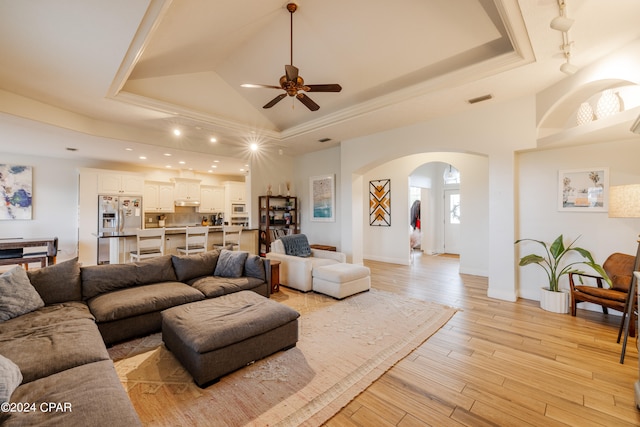 living room with ceiling fan, a tray ceiling, and light hardwood / wood-style floors