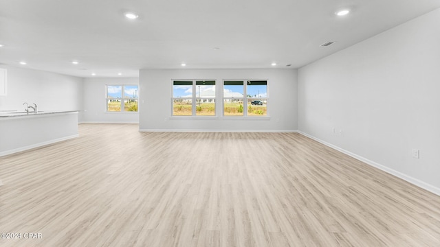 unfurnished living room with baseboards, light wood finished floors, a sink, and recessed lighting